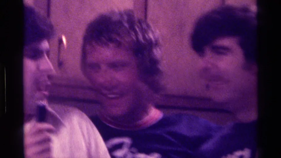In a 1976 Kentucky kitchen scene, three adult men stand shoulder to shoulder as two laugh and one turns toward them.