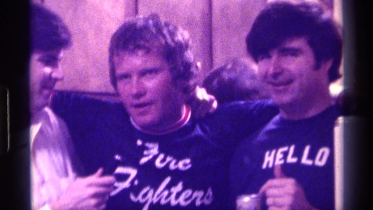 In Kentucky 1976 footage, a female interviewer holds a microphone as two young men stand close together in a casual interior.