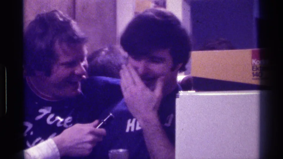 The female interviewer leans in with a microphone as a young man laughs, with a Kodak Ektasound box visible in the 1976 Kentucky interior.