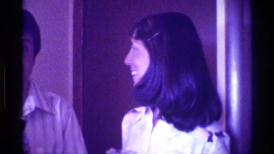 1976 Kentucky home-movie frame of a smiling dark-haired woman in profile during conversation inside a private room.