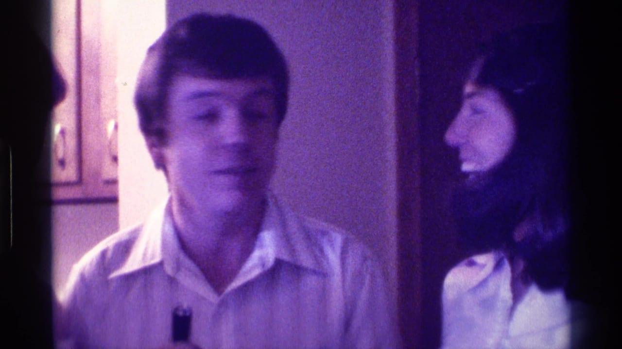 In 1976 Kentucky home-movie footage, a man in a light shirt stands near a woman in a white collared shirt holding a small black microphone.