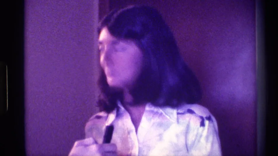 The woman turns in profile with the small black microphone still in hand, framed tightly inside a Kentucky interior in 1976.