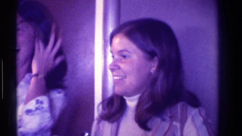 Two adult women appear in a dim 1976 Kentucky interior, with one smiling toward the side and another partly turned while touching her hair.