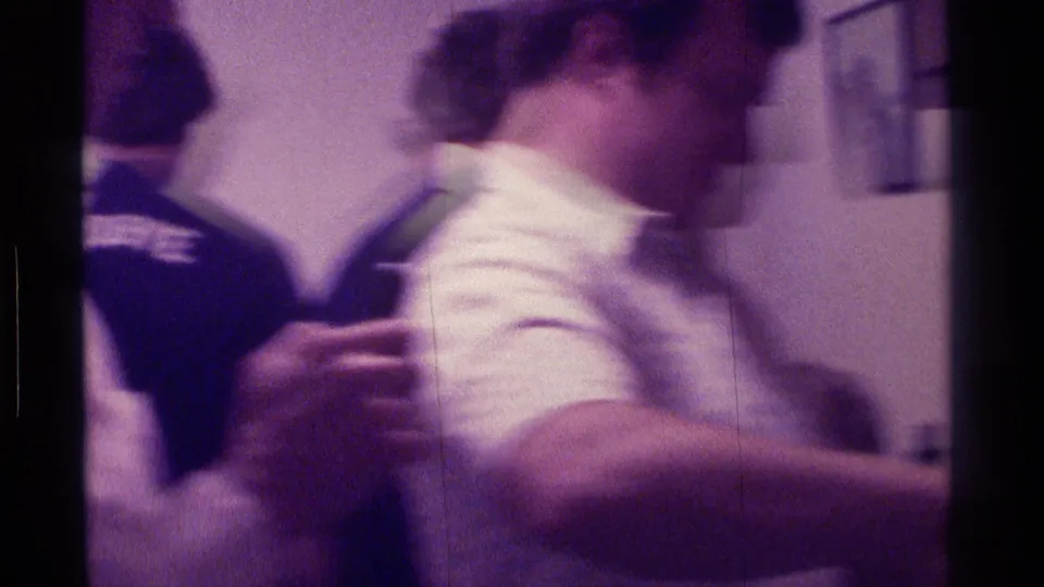 1976 Kentucky party frame showing a man in a white short-sleeved shirt moving past others in a private interior.