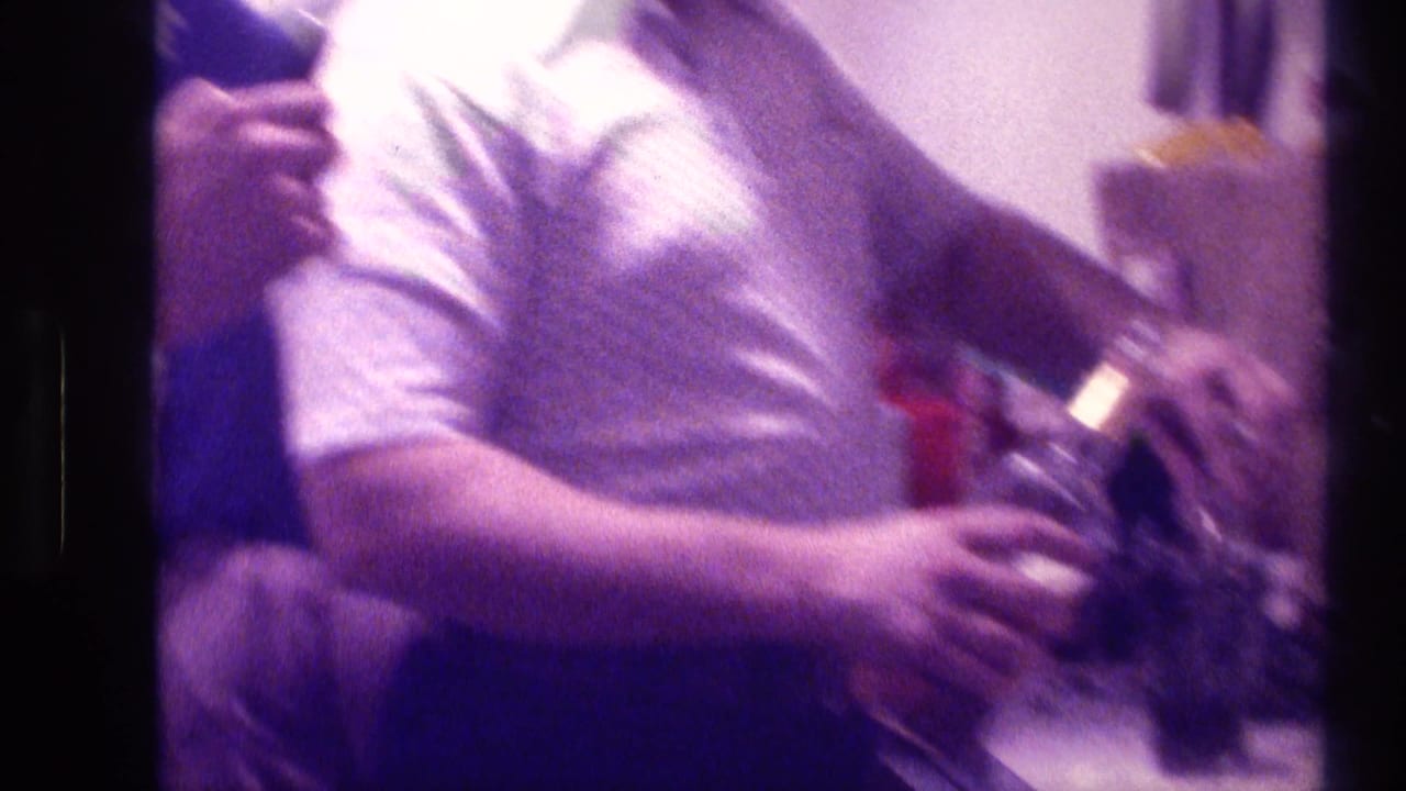 Adult man in a patterned shirt holding a bottle near a crowded counter.