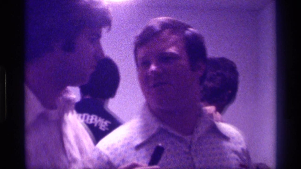 Kentucky 1976 home-movie frame showing a man being interviewed with a microphone while several adults stand in the background.