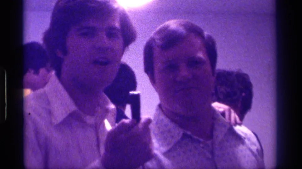 Kentucky 1976 frame with a young man holding a microphone near an older man as people gather in a softly lit interior.