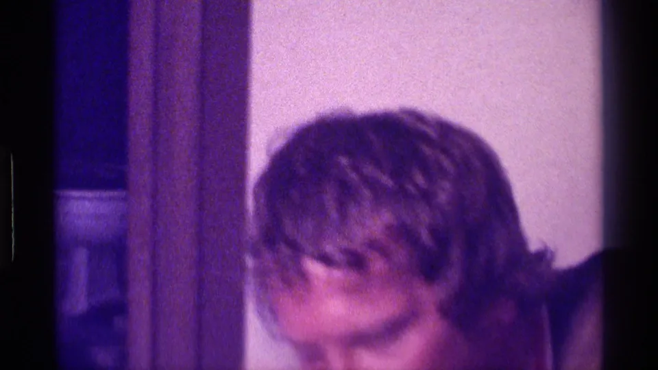Purple-tinted 1976 Kentucky 8mm frame with a partial close view of an adult viewer near interior wood trim.