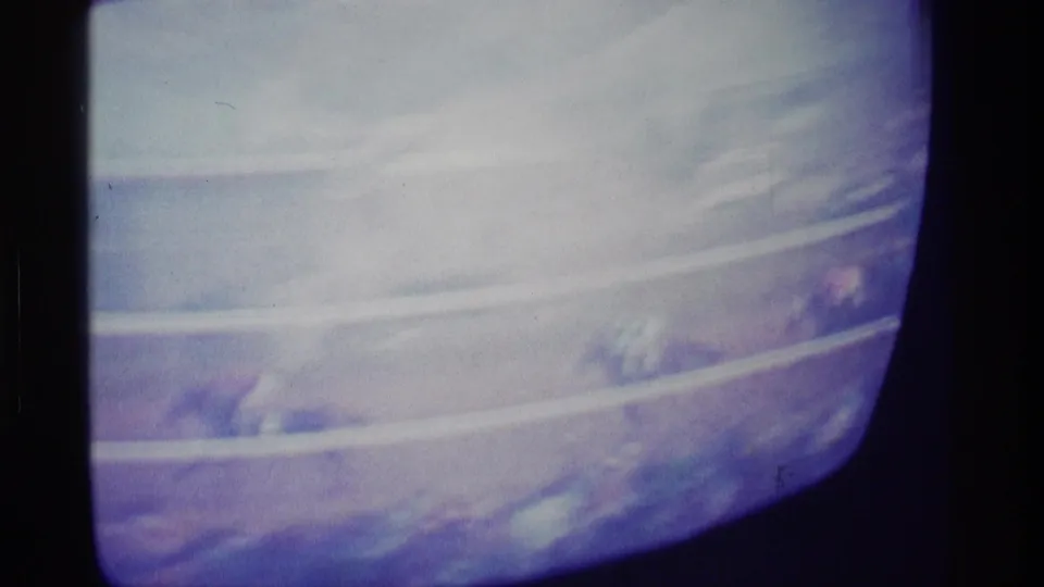 Soft 8mm frame of a CRT television showing a horse race broadcast, with pale rails and small racing figures near the bottom.