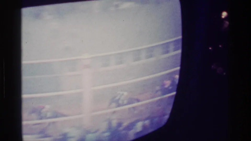 1976 Kentucky home-movie frame of a rounded television screen showing horses and riders on a race track.