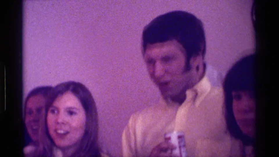 1976 Kentucky 8mm frame showing several adults gathered closely, with a man holding a beer can and women looking toward the camera.