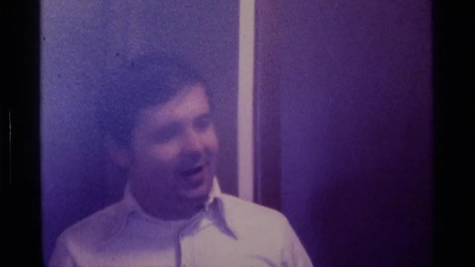 Young white man in a white dress shirt appears indoors in purple-tinted 1976 Kentucky 8mm footage, looking slightly off camera.