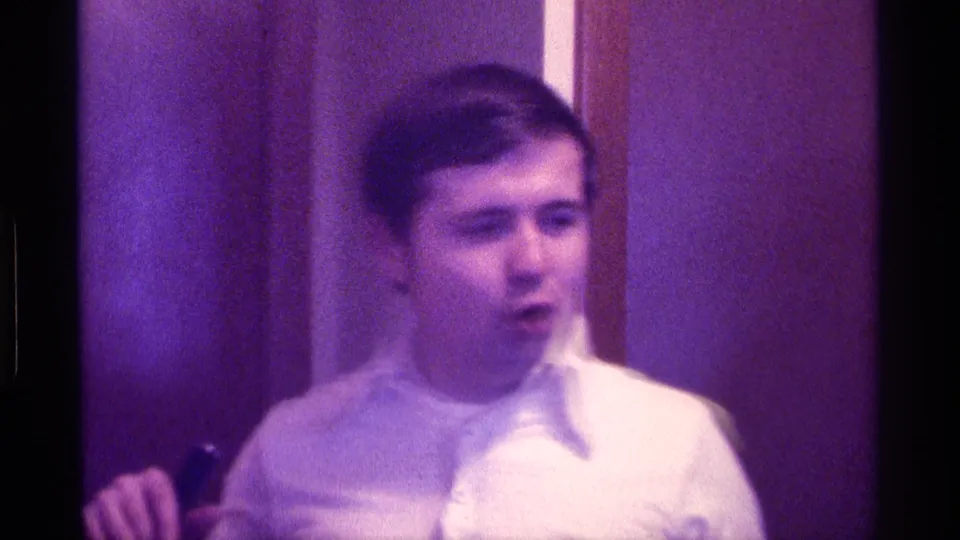 The man appears to speak while holding a dark handheld microphone in the purple-tinted Kentucky interior footage.