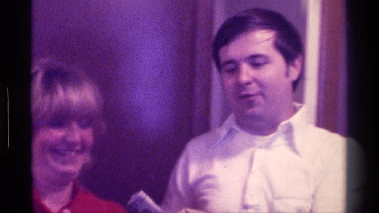 Blonde woman in red beside a man in a white shirt indoors.