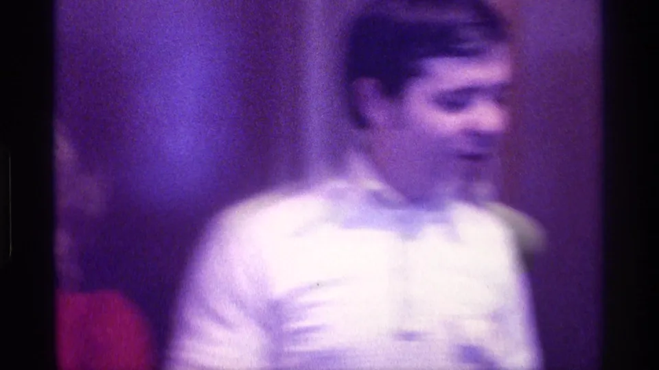 Soft, blurred 1976 Kentucky home-movie frame with a man in a white shirt and a partial view of the woman in red.