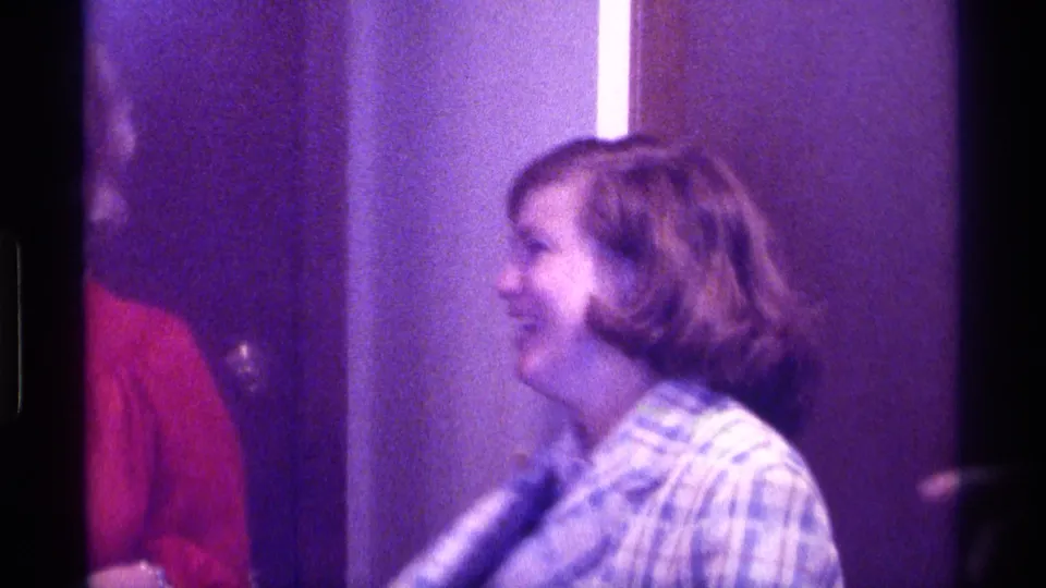 The woman smiles in profile in a dim Kentucky interior, with her plaid blazer still partly visible as she turns.