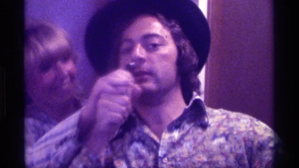 1976 Kentucky 8mm frame with the man centered, holding a microphone near his face as the woman appears partly blurred behind him.