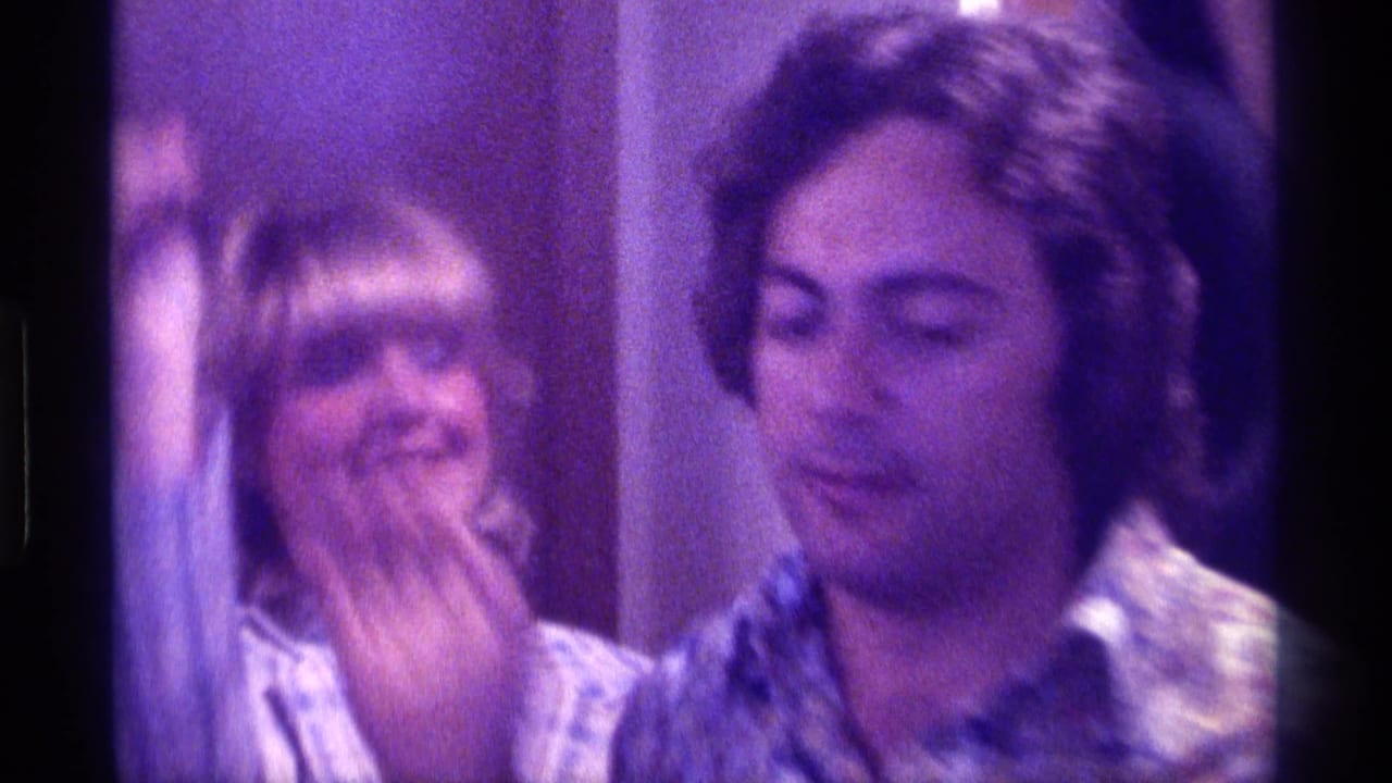 1976 Kentucky 8mm frame showing adults in a dim interior, including a man near a blurred woman in party clothing.