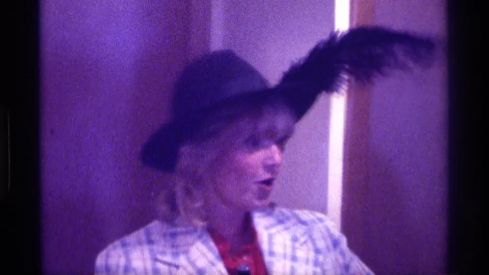 The Kentucky home-movie frame shows the woman turning sideways, with the feather on her dark hat extending across the soft, grainy frame.