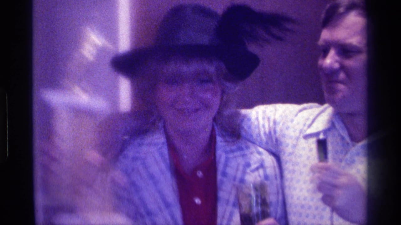 In 1976 Kentucky home-movie footage, a woman in a black hat smiles close to a man holding a microphone at an indoor gathering.