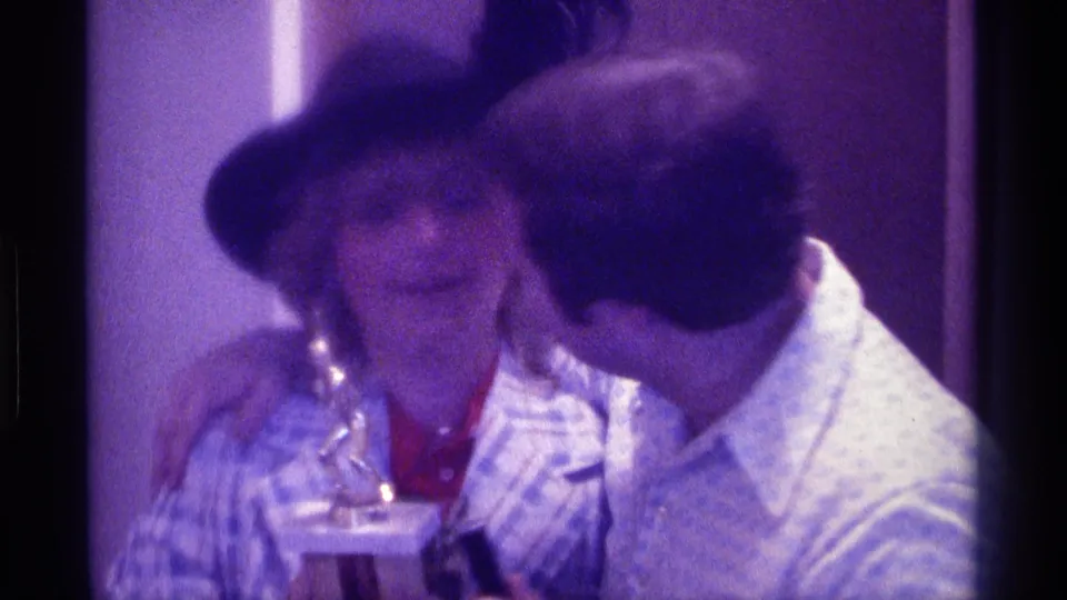 At the end of the 1976 Kentucky home-movie clip, the man kisses the woman in a black hat as she holds a drink indoors.