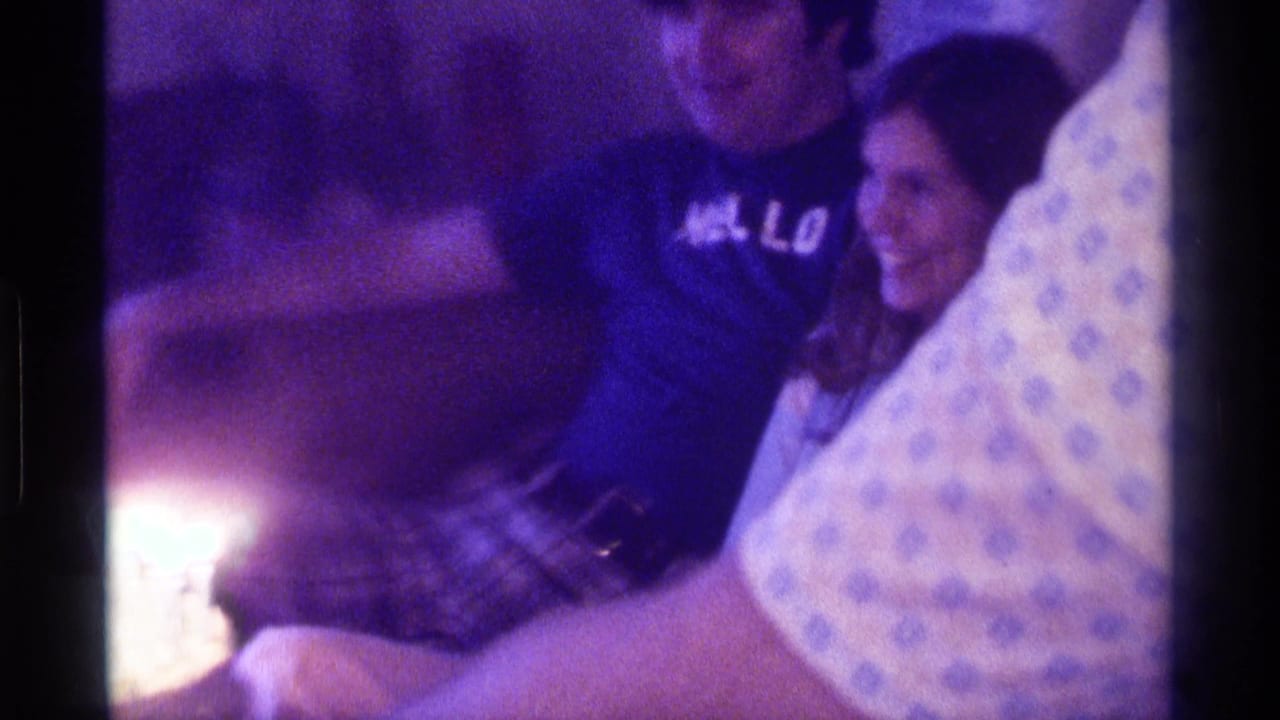 A woman smiles beside a man as bright birthday candles glow at the edge of the frame.