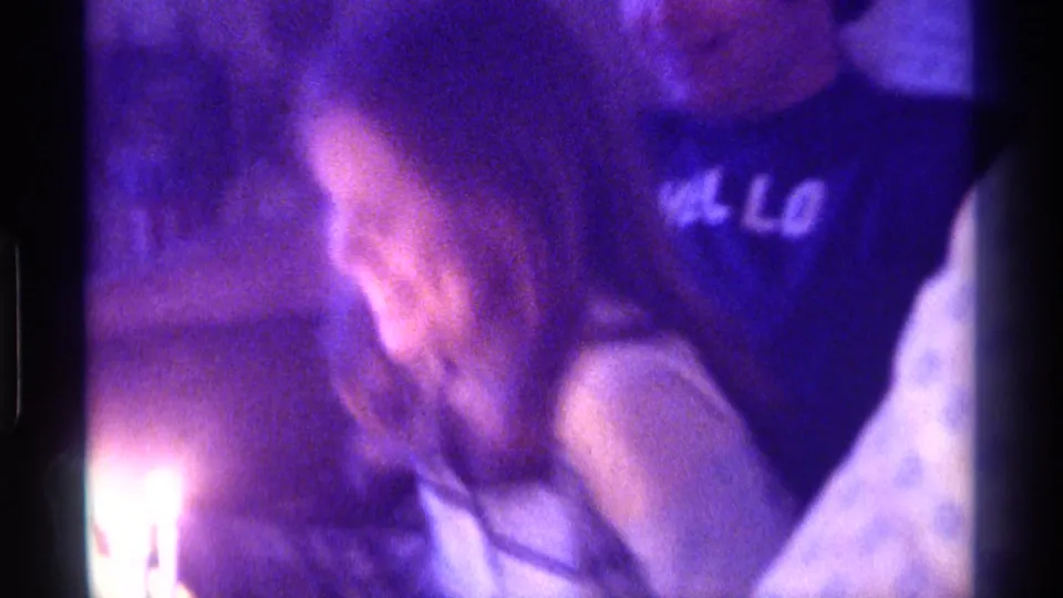 The woman leans forward toward glowing birthday candles, with the man in the dark shirt partly visible behind her.