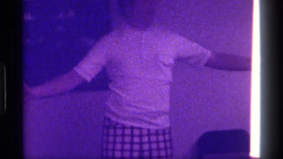 1976 Kentucky home-movie frame of a person in a white shirt extending both arms in a dim private living room.