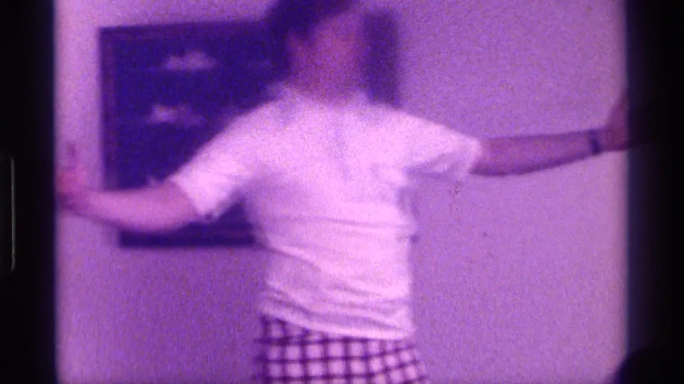 Purple-tinted 8mm frame from 1976 Kentucky showing a person moving with one arm extended near framed wall art.