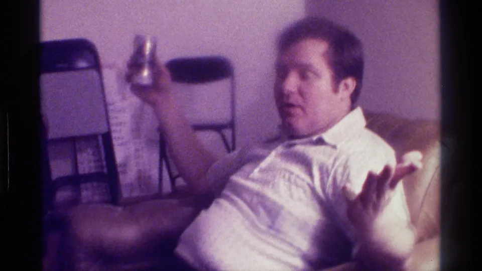 The man remains seated in the recliner, holding a beer can near his shoulder while his open hand faces the camera in a casual indoor 1976 Kentucky home-movie scene.