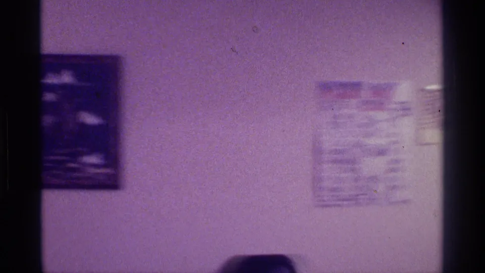 Home-movie view of a living room wall in Kentucky with framed art, a calendar, pale wall, and furniture partly visible below.