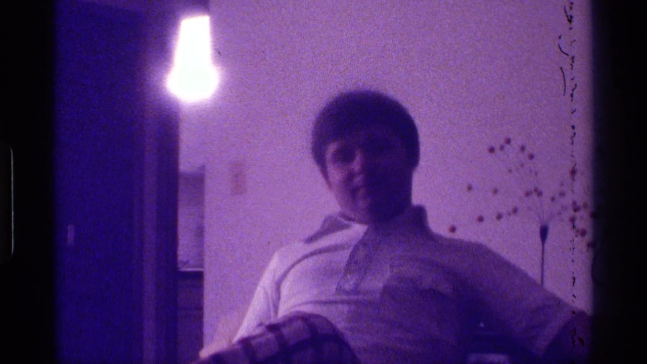 Young man seated on a couch in a dim room under a bright hanging light.