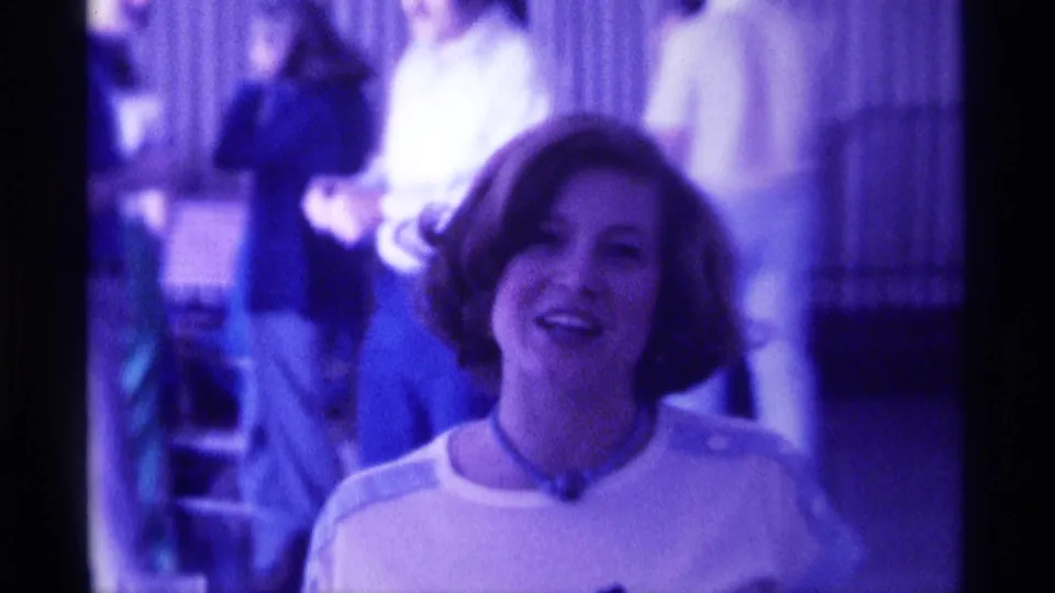 The woman continues smiling and appears to speak directly to the camera, with adults visible behind her in the Kentucky indoor scene.