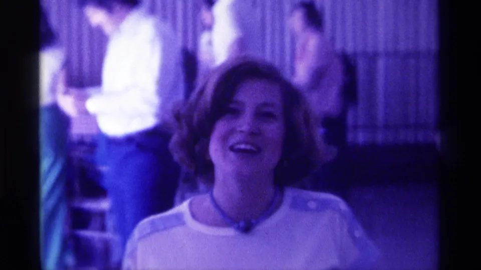 The woman looks upward toward the camera with a broad smile, surrounded by softly focused background guests in 1976 Kentucky footage.