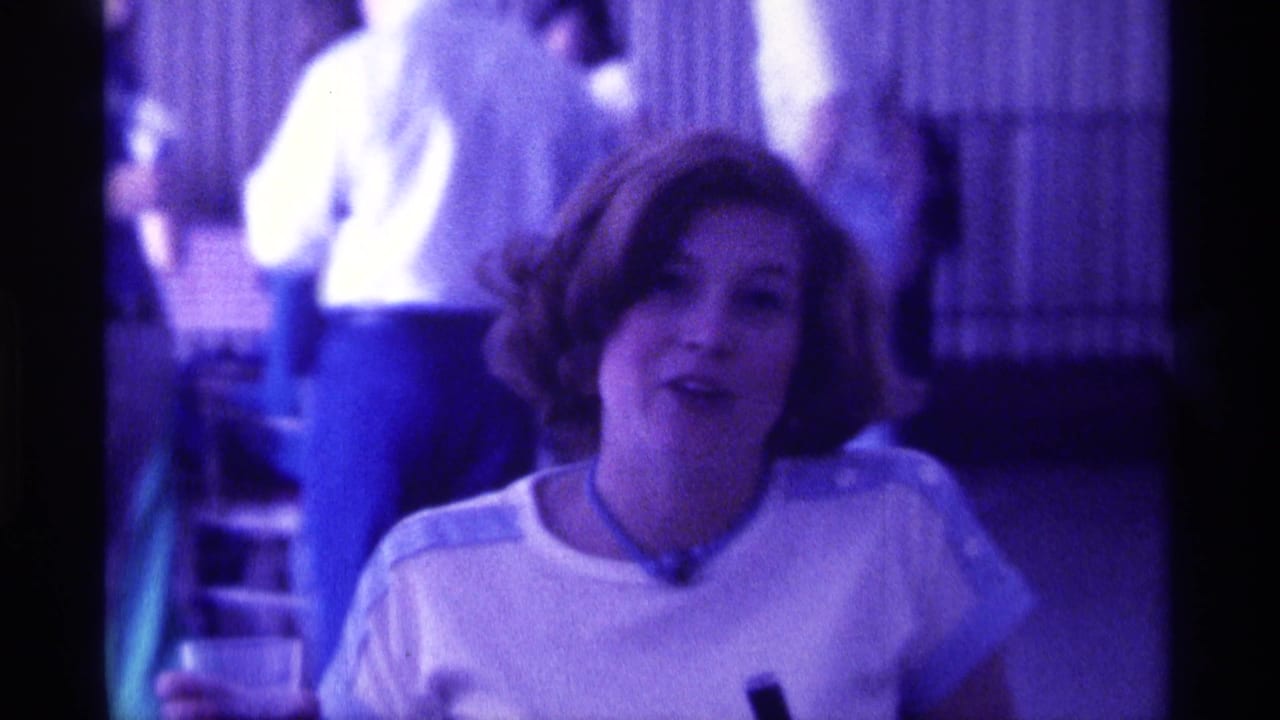 In 1976 Kentucky home-movie footage, a young woman with a bob haircut speaks toward the camera in a dim indoor room.