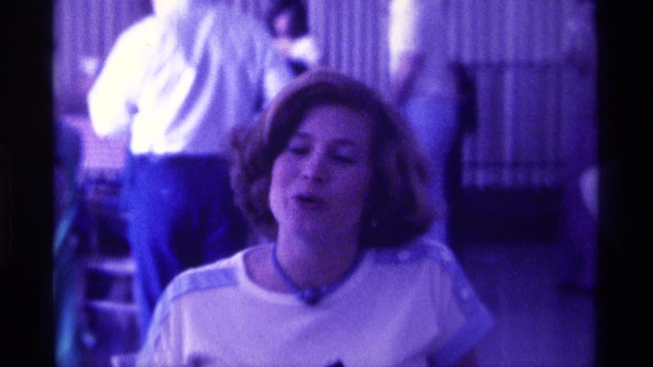 Woman in a white top faces the camera with adults standing behind her indoors.