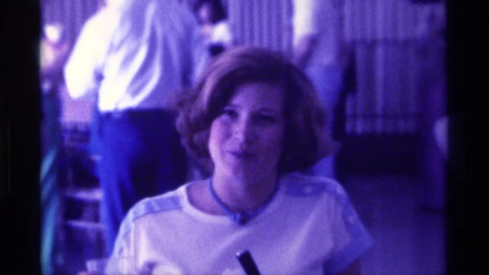 The woman smiles toward the camera as a small dark microphone is partly visible near the bottom of the frame.