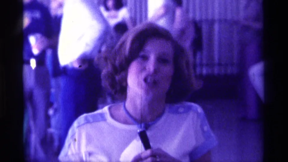 The woman appears mid-speech with a microphone, surrounded by adults at an indoor Kentucky gathering in 1976.