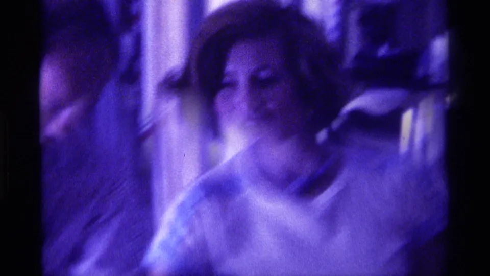 A motion-blurred 8mm frame shows the woman and nearby guests during the indoor social moment in Kentucky, 1976.