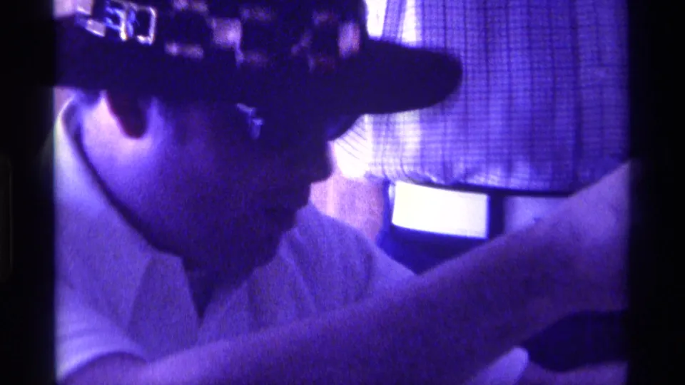 Adult man in a dark cowboy hat and light collared shirt looks down in a purple-tinted 1976 Kentucky home-movie frame.