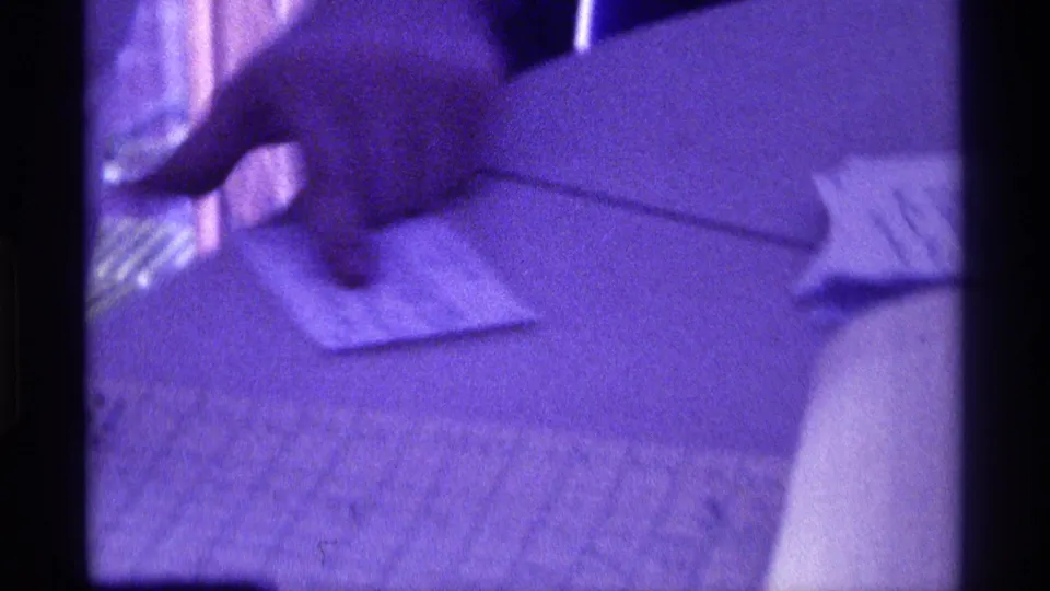 A hand rests near or points to a small notepad on a table, with strong purple-blue color from the 8mm scan.