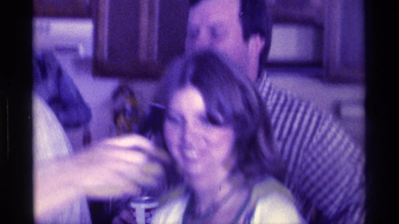 Adults gathered indoors as a woman holds a cup near a man in a striped shirt.