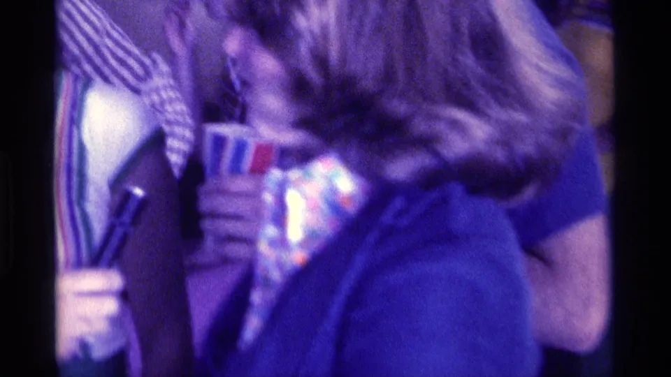 1976 Kentucky home-movie frame of a woman at a crowded indoor party turning toward a handheld microphone.