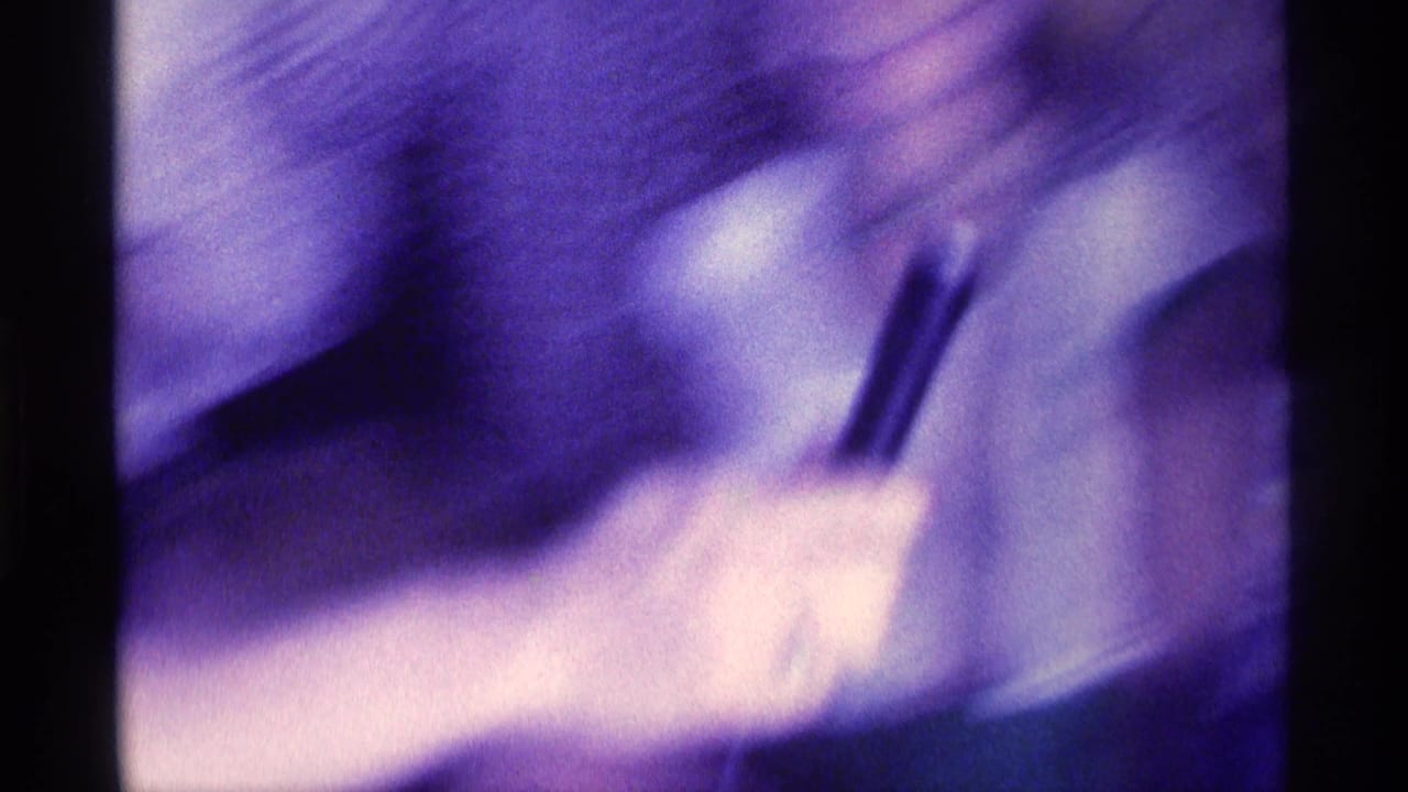 Blurred close-up of a hand holding a dark bottle or glass in purple-tinted party footage.