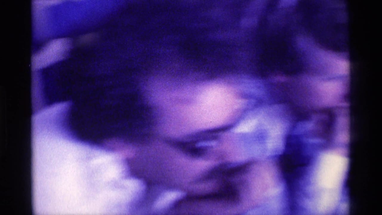 Soft, purple-tinted close view of an adult man leaning forward in a crowded room.