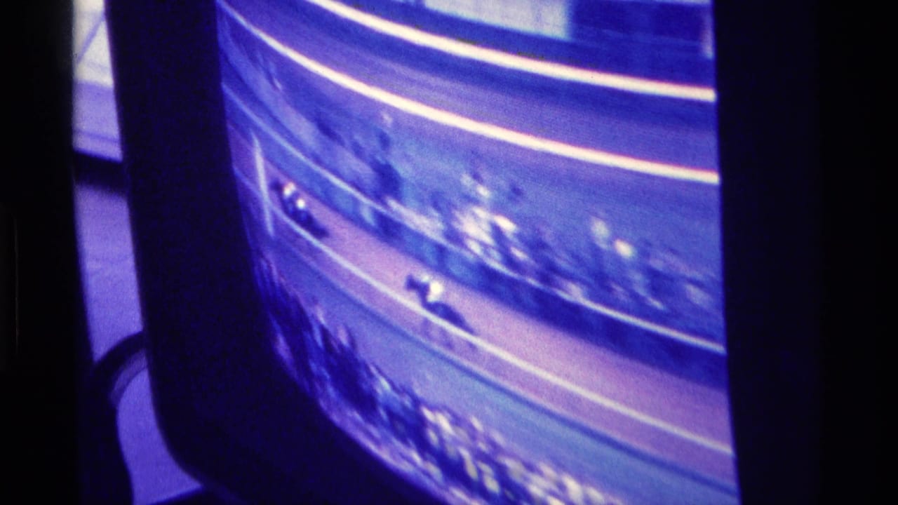 1976 Kentucky home-movie frame of a color television showing horses on a dirt racetrack with blue-purple cast and blurred spectators.