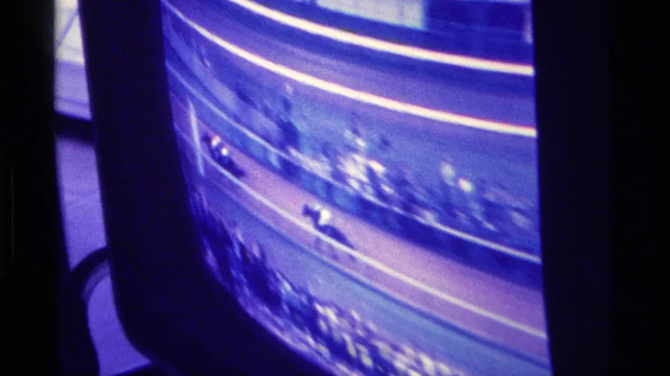 1976 Kentucky home-movie frame of a color television showing horses on a dirt racetrack with blue-purple cast and blurred spectators.