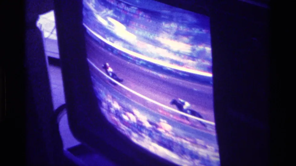Final 1976 Kentucky home-movie frame shows horses on a televised dirt track, with strong screen glare and purple-blue film color.