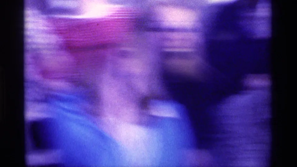 Motion-blurred 1976 Kentucky frame of a woman in blue moving among adults in a crowded indoor home-movie scene.