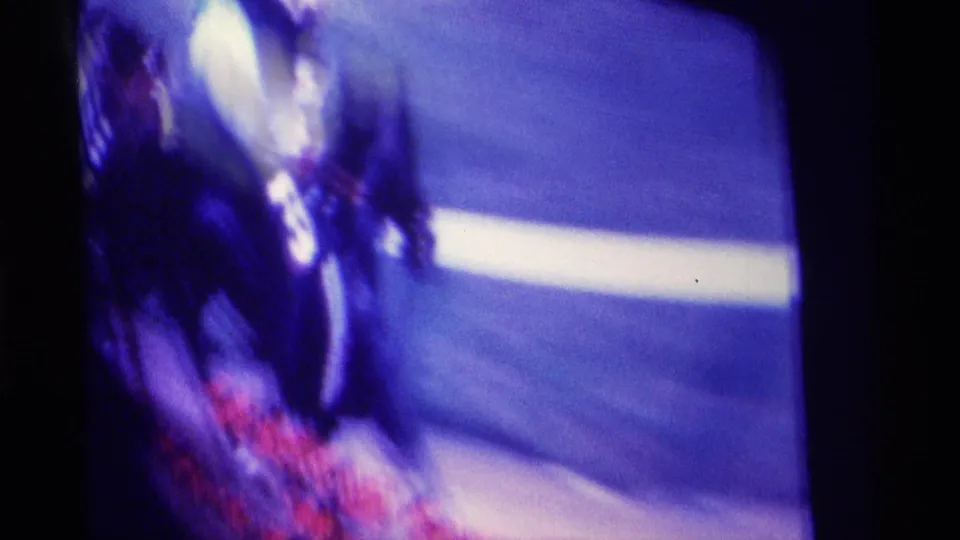 Purple-tinted television frame shows a blurred horse-racing broadcast with track area, bright highlights, and red text near the lower edge.